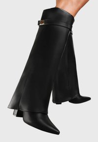 Bottes de cheville en cuir noir avec une silhouette ajustée, des orteils pointus et un accent de boucle amovible, dotées d'une fermeture éclair latérale pour un enfilage facile.