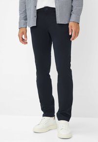 Marineblaue Stretch-Hosen im Slim Fit mit einem Frontknopfverschluss und Taschen, kombiniert mit weißen Sneakers und einem karierten Hemd.