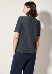 Marineblauwe T-shirt met korte mouwen en een textuurgebreid ontwerp. Rechte snit, ronde halslijn en een relaxte pasvorm, gecombineerd met donkere broeken.