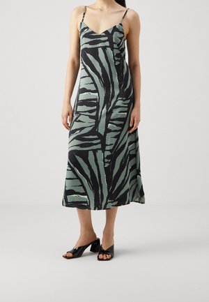 Kvinde iført en ærmeløs midi-kjole med sorte og grå zebra-striber, tynde stropper og sorte blokhælede sandaler med åbne tæer.