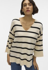 Maglione a righe beige e nero con scollo a V, maniche a tre quarti e vestibilità morbida, caratterizzato da un tessuto testurizzato.
