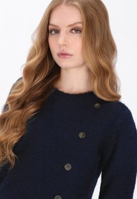 Marine uldblandings sweater med rund halsudskæring, der har to dekorative brune knapper foran og en blød, struktureret overflade.