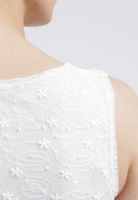 Weißes ärmelloses Top mit einem strukturierten floralen Stickmuster, das geschwungene Linien und kleine Blumenakzente aufweist, aus leichtem Stoff.