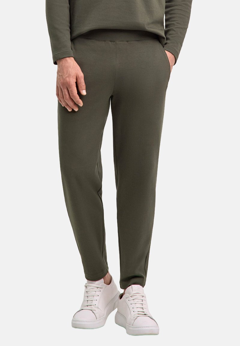 Olivgrüne, gerippte Jogginghosen mit schlankem Schnitt, Seitentaschen und bequemem Bund, kombiniert mit weißen Sneakers.