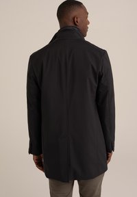 Abrigo negro con un alto collar, corte estructurado y tela suave, con costuras ajustadas y puños abotonados. Se muestra la vista trasera.