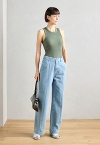Zelený žebrovaný top, světle modré široké džíny a otevřené modré podpatky. Rukávová černá taška, minimalistický design a přiléhavý silueta.