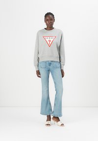 Grijze katoenen sweatshirt met een rood driehoekig logo, gecombineerd met lichtblauwe flare jeans. Lichtgekleurde, hoge hakken ronden de look af.