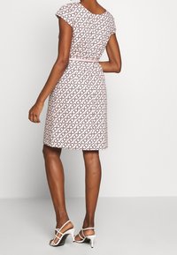 Robe ajustée à manches courtes de couleur rose clair avec un motif répétitif de logos noirs, cintrée à la taille, se terminant juste au-dessus du genou.