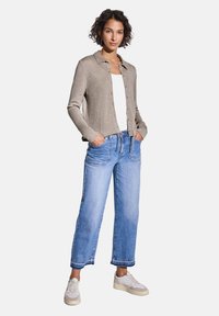 Gilet gris clair avec un col et une fermeture à boutons, associé à un jean denim bleu clair à coupe décontractée et des baskets blanches. Design simple.