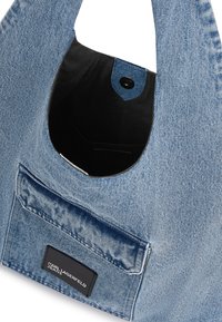 Saco de denim com bolso frontal apresentando o rótulo Karl Lagerfeld Jeans, fecho de botão de pressão preto e forro interior preto.