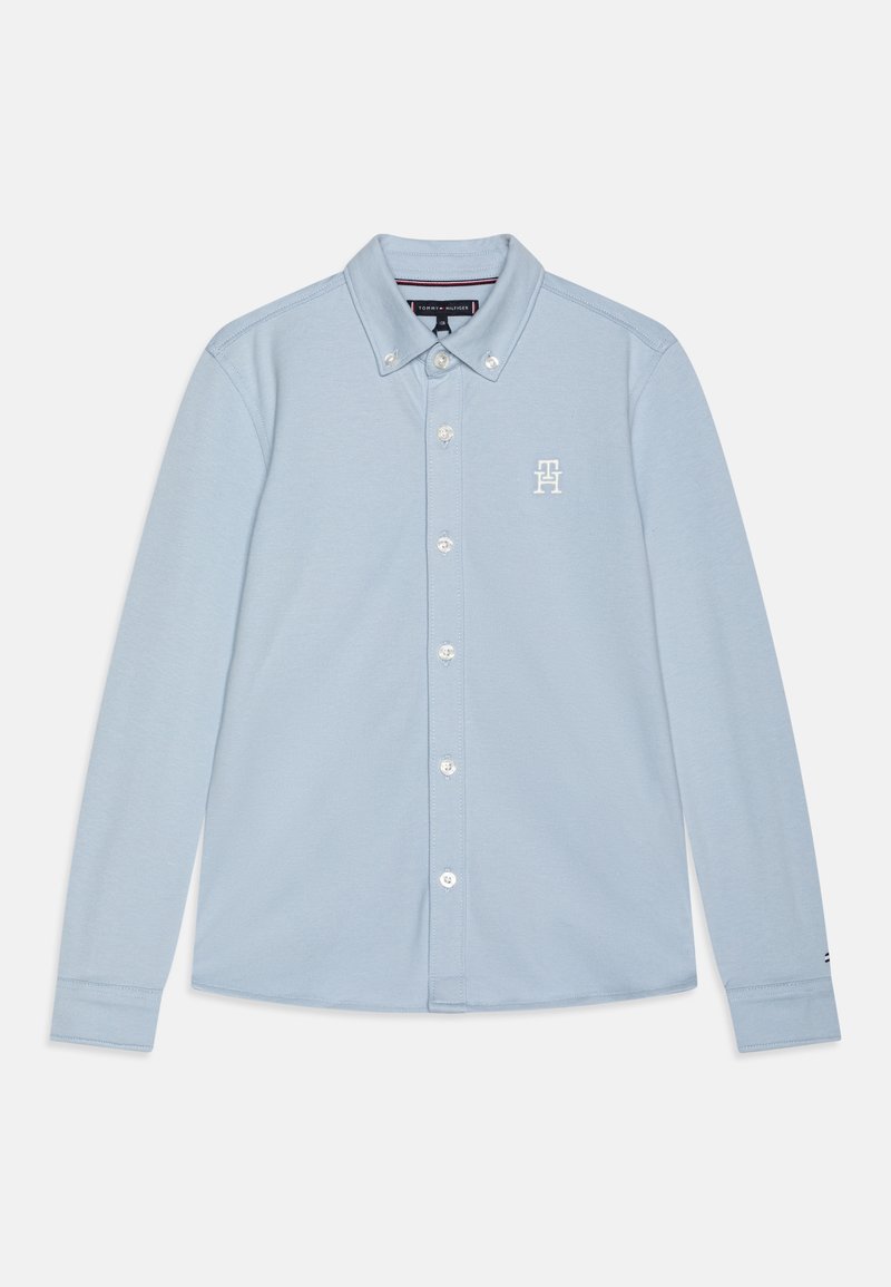 Chemise bleu clair à manches longues, boutonnée, avec col et petit logo blanc brodé sur la poitrine gauche.
