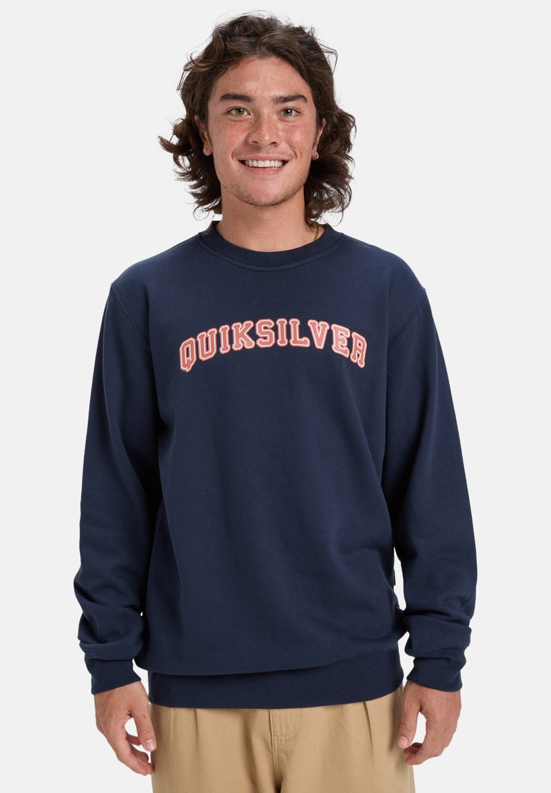 Námornícky modrý mikina vyrobená z bavlneného zmesi, s okrúhlym výstrihom a dlhými rukávmi. Na hrudi je nápis "QUIKSILVER" v zakrivenom, svetlooranžovom písme.