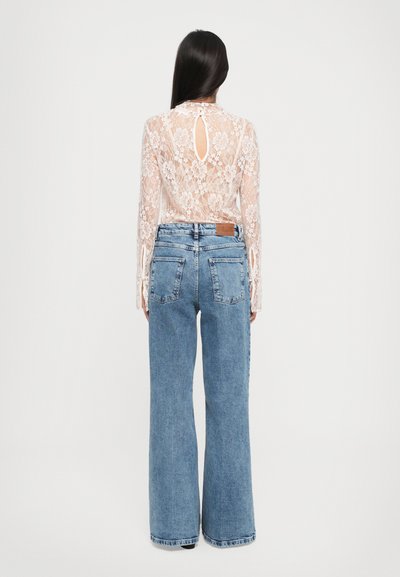 Top de encaje de manga larga con patrones florales y abertura en la espalda, combinado con jeans de mezclilla azul de pierna ancha, de tiro alto y con bolsillos traseros.