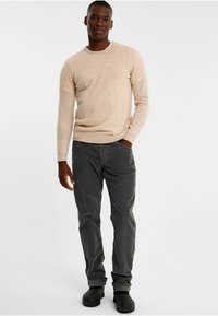 Beige tröja gjord av mjukt material, ihopparad med mörkgrå byxor. Klädseln har en enkel design med rund hals och rak passform.
