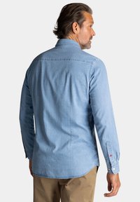 Lichtblauwe denim shirt met lange mouwen, een kraag en knoopsluitingen. Heeft een gebogen zoom en contrasterende knoopaccenten.