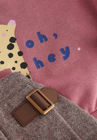 Sudadera rosa con un diseño de leopardo amarillo y texto azul "oh, hey." Abajo, una tela de pata de gallo texturizada con un acento de cinturón marrón.