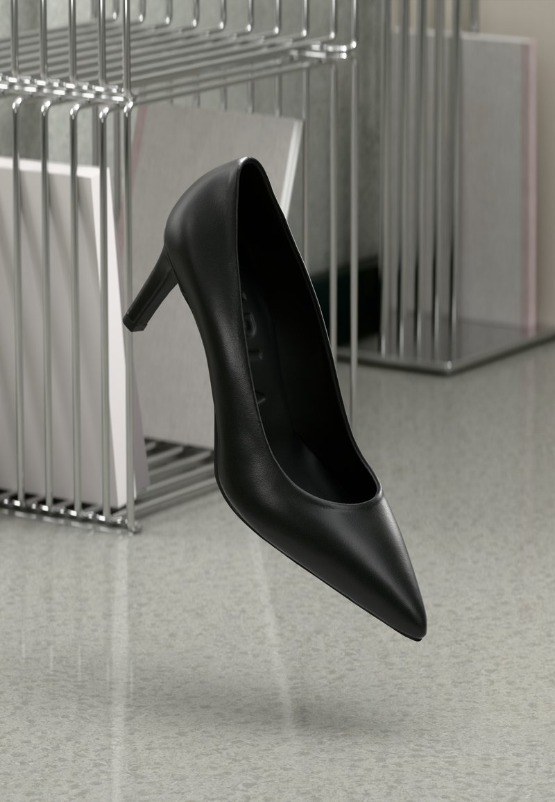 Sapato de salto alto em couro preto com bico fino e um salto esbelto, contra um fundo minimalista com metal e cores neutras.