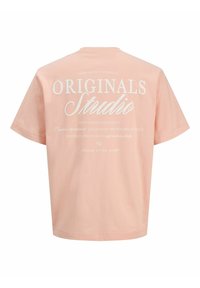 Ροδακινί βαμβακερό t-shirt με κοντά μανίκια, που φέρει μεγάλο άσπρο κείμενο στην πλάτη: "ORIGINALS Studio" και επιπλέον μικρότερα κείμενα.