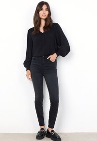 Svart blus med långa ärmar och knappslå, elastiska ärmslut, kombinerad med svarta tajta jeans och svarta loafers med detaljer i guld.
