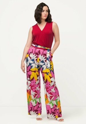 Top rosso senza maniche abbinato a pantaloni larghi con motivo floreale che presenta tonalità di rosa, giallo e blu, con un dettaglio in vita legato.