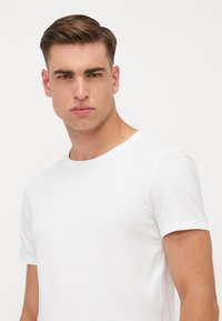 White short-sleeve t-shirt made of smooth fabric. Crew neck design, fitted shape, and minimalist style with no visible logos or patterns.