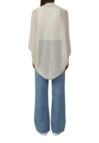Leichter, beiger Mesh-Cardigan mit lockeren, langen Ärmeln und einem abgerundeten Saum, kombiniert mit lockeren Jeans aus Denim.