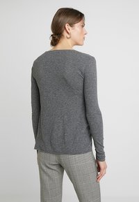 Pilkos spalvos ilgarankovė marškinė pagaminti iš minkštos, lengvos medžiagos su apvalia apykakle. Dėvimi su raštuotomis kelnėmis, pabrėžiančiomis atsipalaidavusią išvaizdą ir paprastą dizainą.