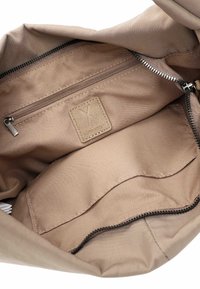 Binnenkant van een beige stoffen tas met een ritssluitingvak, een open vak en een gestikte merkembleem.