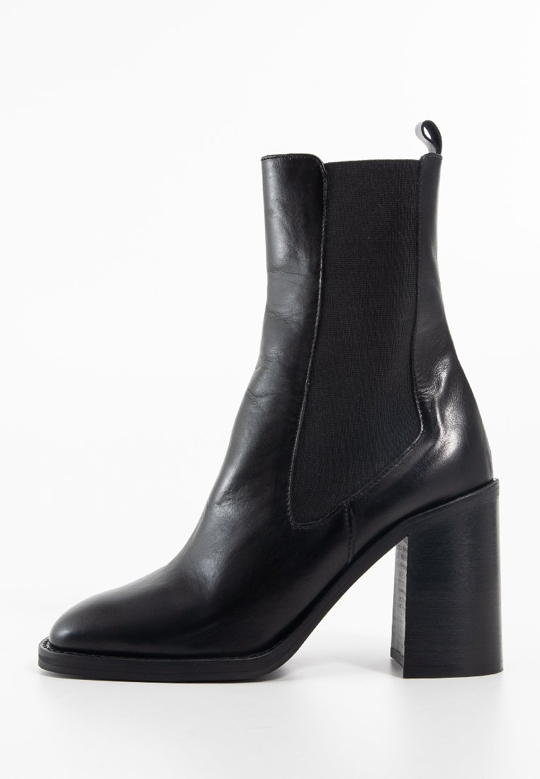 Bottine en cuir noir avec des panneaux latéraux en élastique, bout pointu et talon épais. Texture lisse avec une silhouette élégante.