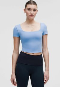 Helles blaues Cropped-Top mit kurzen Ärmeln und einem quadratischen Ausschnitt, kombiniert mit schwarzen, hoch taillierten Leggings aus glattem Stoff.