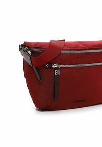 Sac en nylon rouge à bandoulière avec une texture lisse, comportant une fermeture éclair argentée, des accents en cuir marron et une sangle ajustable.
