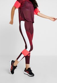 Urheiluasu, jossa on marjapuuron värinen verkkopaita vaaleanpunaisin yksityiskohdin ja istuvat marjapuuronväriset leggingsit, joissa on valkoiset paneelit ja vaaleanpunaiset resorit, yhdistettynä mustiin lenkkareihin.