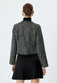 Giacca in tweed bianca e nera con un design cropped, maniche lunghe e colletto a coste nero. Abbinata a una gonna plissettata nera.