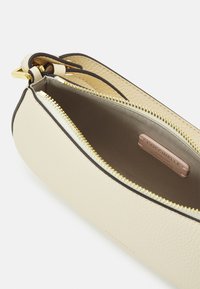 Borsa a mano in pelle beige con cerniera dorata, tracolla regolabile e interno in tessuto beige con etichetta del marchio cucita.