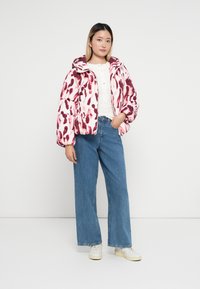Geacă puffer roz și albă cu un model cu pete, având glugă. Combinată cu blugi largi blue și adidași albi.