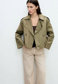 Cropped olive-green jacket with a wide collar and double-breasted buttons, paired with light beige wide-leg trousers. Smooth fabric texture.