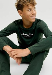 Roheline pikkade varrukatega särk ja pükste komplekt, valmistatud pehmest kangast. Särgil on rinnal valge logo "Jack & Jones". Lihtne disain, kinnitatud lõige.