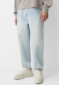Lysblå denimjeans med en afslappet pasform, der har falmede lapper, lige ben og er parret med off-white sneakers.