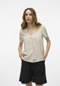 Top beige de manga corta con escote en V y detalle de pliegues, combinado con pantalones cortos negros de cintura alta, que presentan un ajuste relajado y una textura suave.