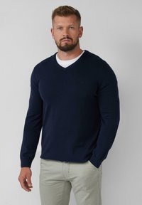 Navy blauwe v-hals trui van een glad gebreide stof, met lange mouwen en een getailleerd ontwerp, gecombineerd met lichtgekleurde broek.