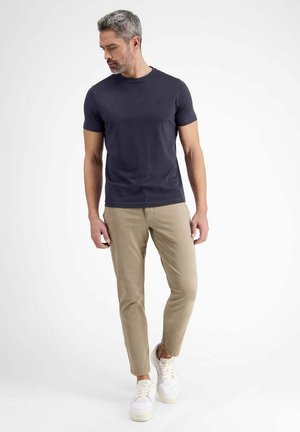 Marineblaue Baumwoll-T-Shirt mit kurzen Ärmeln, kombiniert mit hellbeigen Hosen und weißen Sneakers, im Slim-Fit-Schnitt und mit minimalistischem Design.