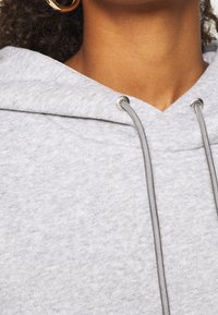 Sudadera con capucha gris de textura suave, con una gran capucha y ojales plateados para los cordones. Diseño simple y casual.