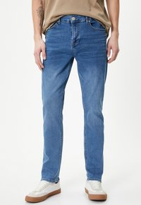 Jeans in denim blu con vestibilità dritta, design a cinque tasche e zip, abbinati a sneaker bianche e beige. Tessuto morbido.