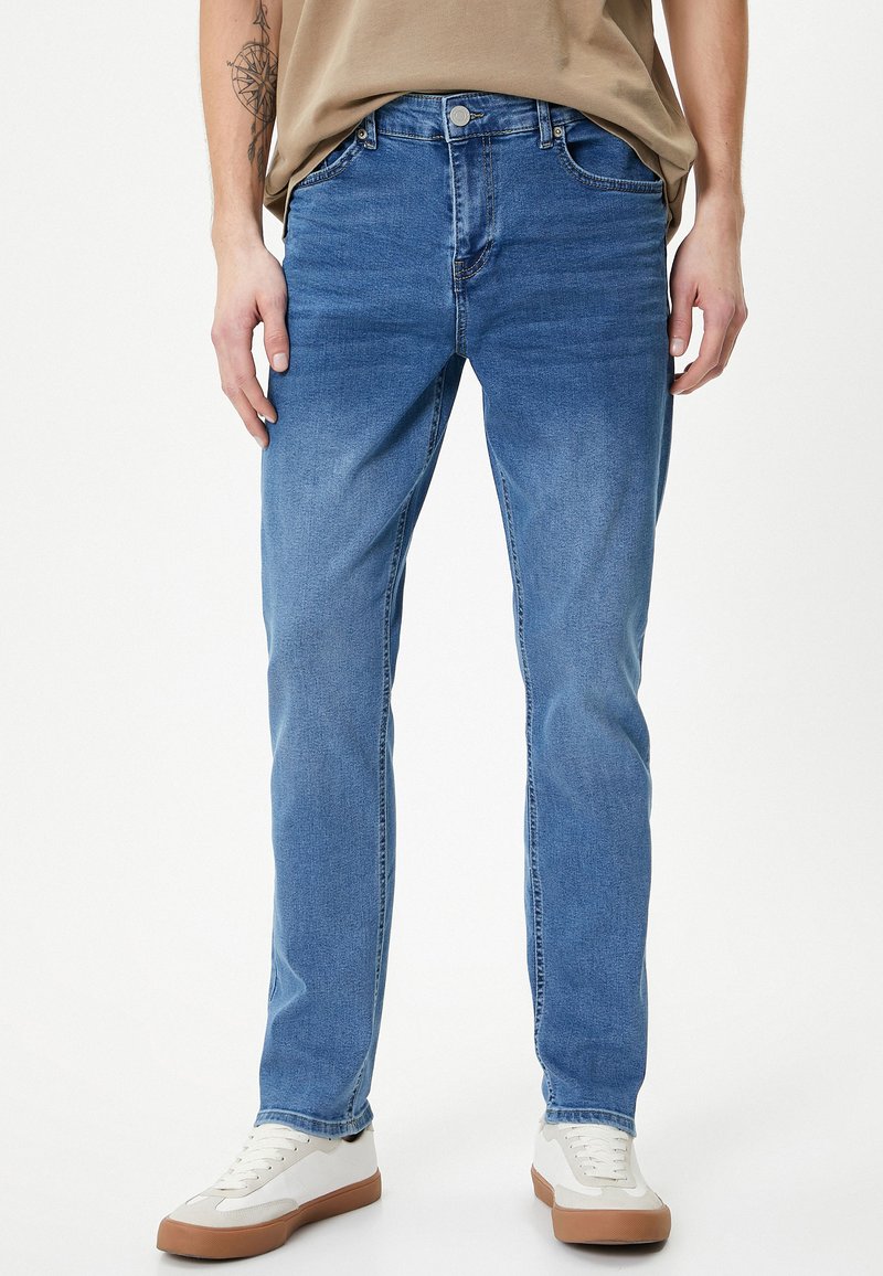 Jeans in denim blu con vestibilità dritta, design a cinque tasche e zip, abbinati a sneaker bianche e beige. Tessuto morbido.