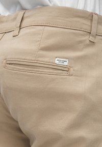 Beige trousers with a smooth cotton texture, featuring a rear pocket and a small label reading "JACK & JONES EST. 1990."