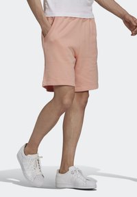 Broskvové bavlněné kraťasy s uvolněným střihem, bočními kapsami a hladkým texture, v kombinaci s bílými teniskami.