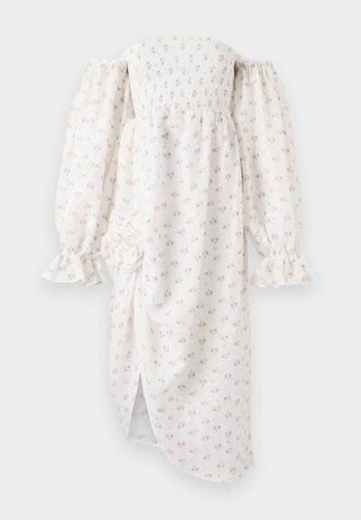 White off-the-shoulder dress with smocked bodice, long puff sleeves, floral pattern, ruffled cuffs, and a side slit. Features a fabric flower detail.