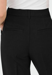 Zwarte op maat gemaakte broek met een gladde textuur, een aangesloten taille en twee achterzakken met minimale stikseldetails.
