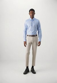 Šviesiai mėlyna marškinėliai su sagomis, kreminės kelnės, rudas diržas, juodi batai. Modelis stovi tiesiai, demonstruodamas prigludusią konstrukciją. Lygus audinys, subtilios detalės.