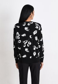 Svart tröja med ett blommönster i vitt, med ribbat nederkant och ärmar. Designen har en avslappnad passform och långa ärmar.